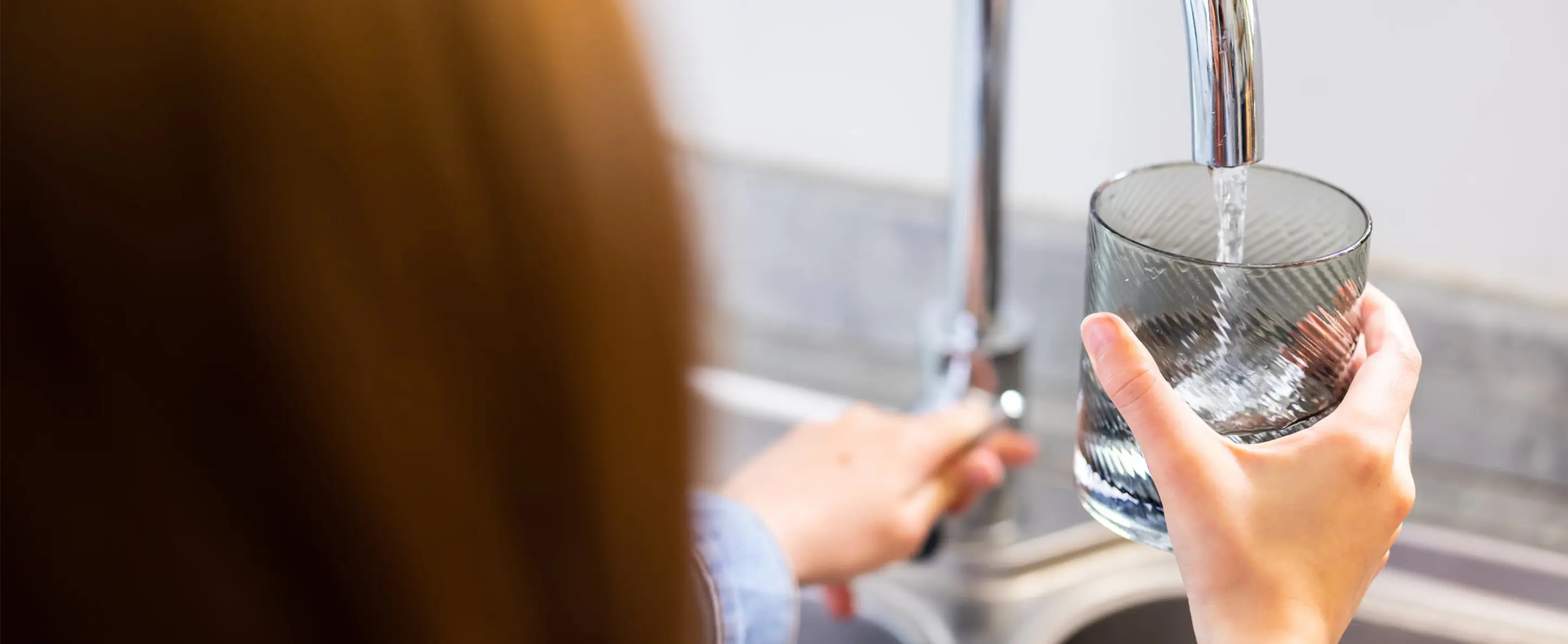 back of a young girl getting a drink of water from tap